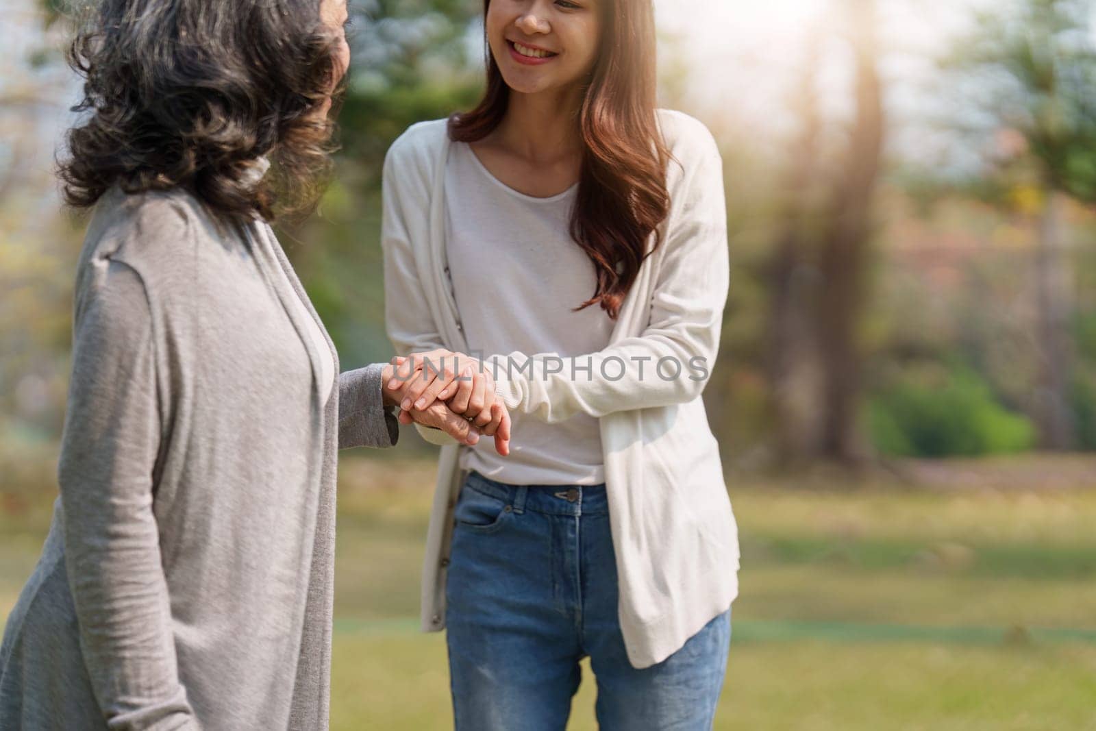 Close up of Adult daughter holding her elderly mother hand with love and walk together.