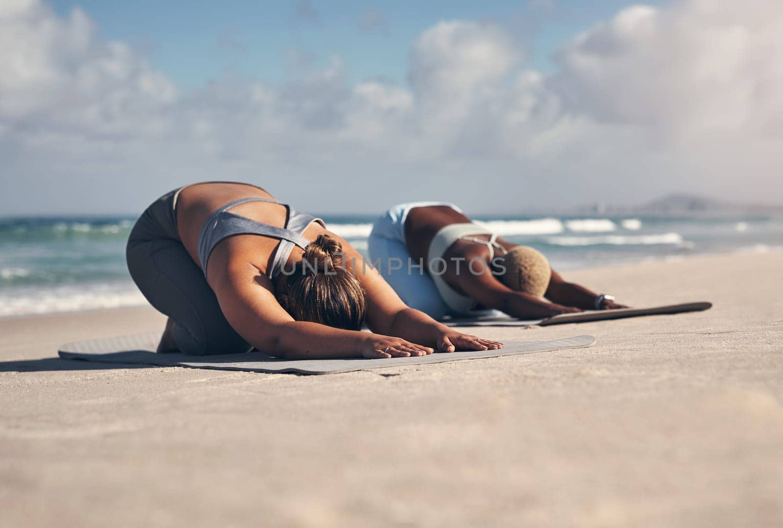 Yoga is one type of medicine thatll solve all your problems. two young women practicing yoga on the beach. by YuriArcurs