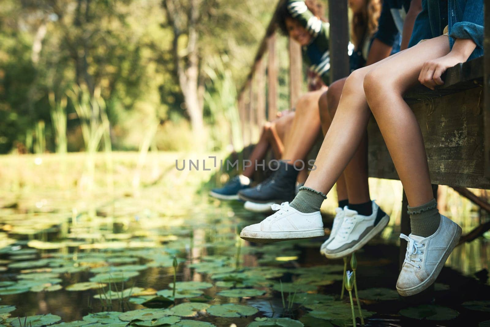 Summer days spent down at the creek. a group of unrecognisable teenagers sitting on a bridge in nature at summer camp. by YuriArcurs