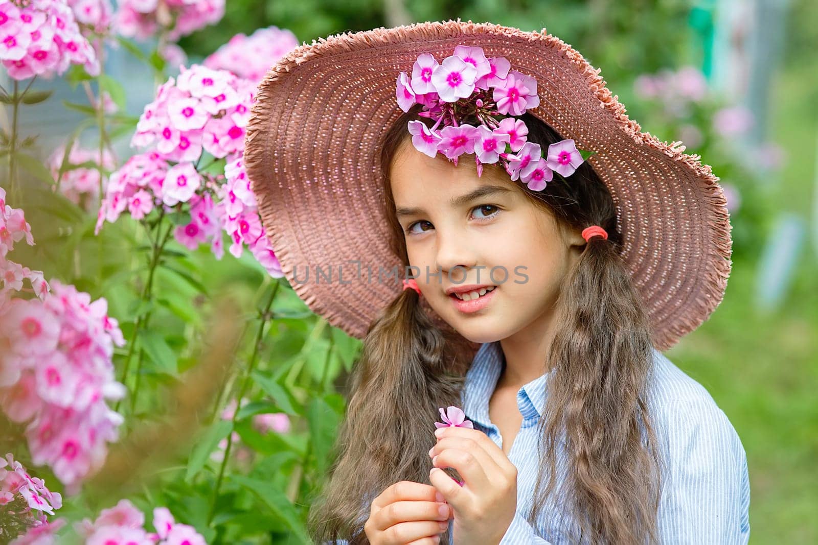 Portrait of a cute little girl in hat with pink phlox flowers, summer. Close up