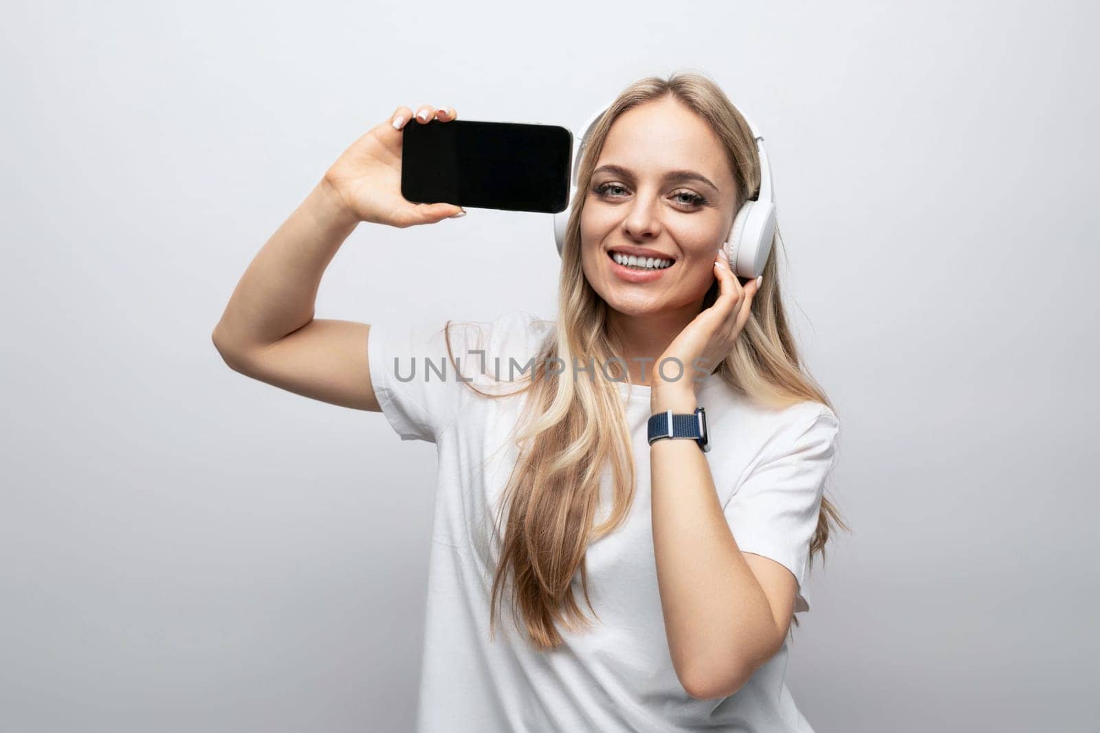 girl in wireless headphones with a smartphone mockup in her hands on a white background.