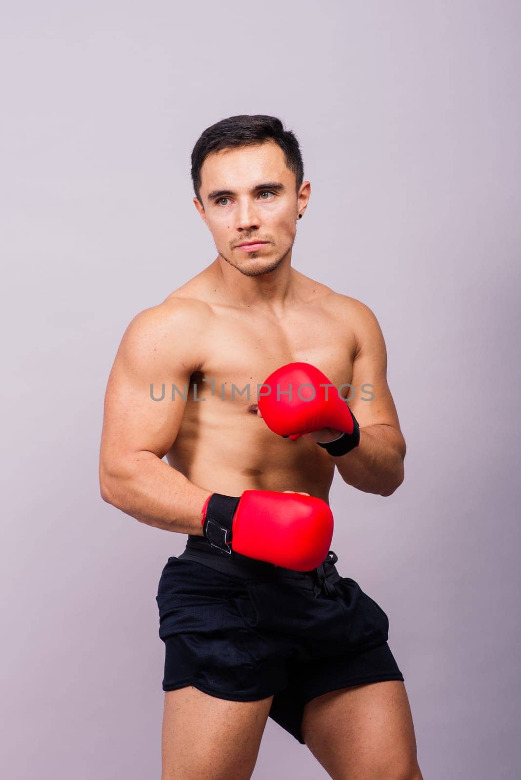 Muscular model sports young man in a boxing gloves on grey background. Male flexing his muscles.