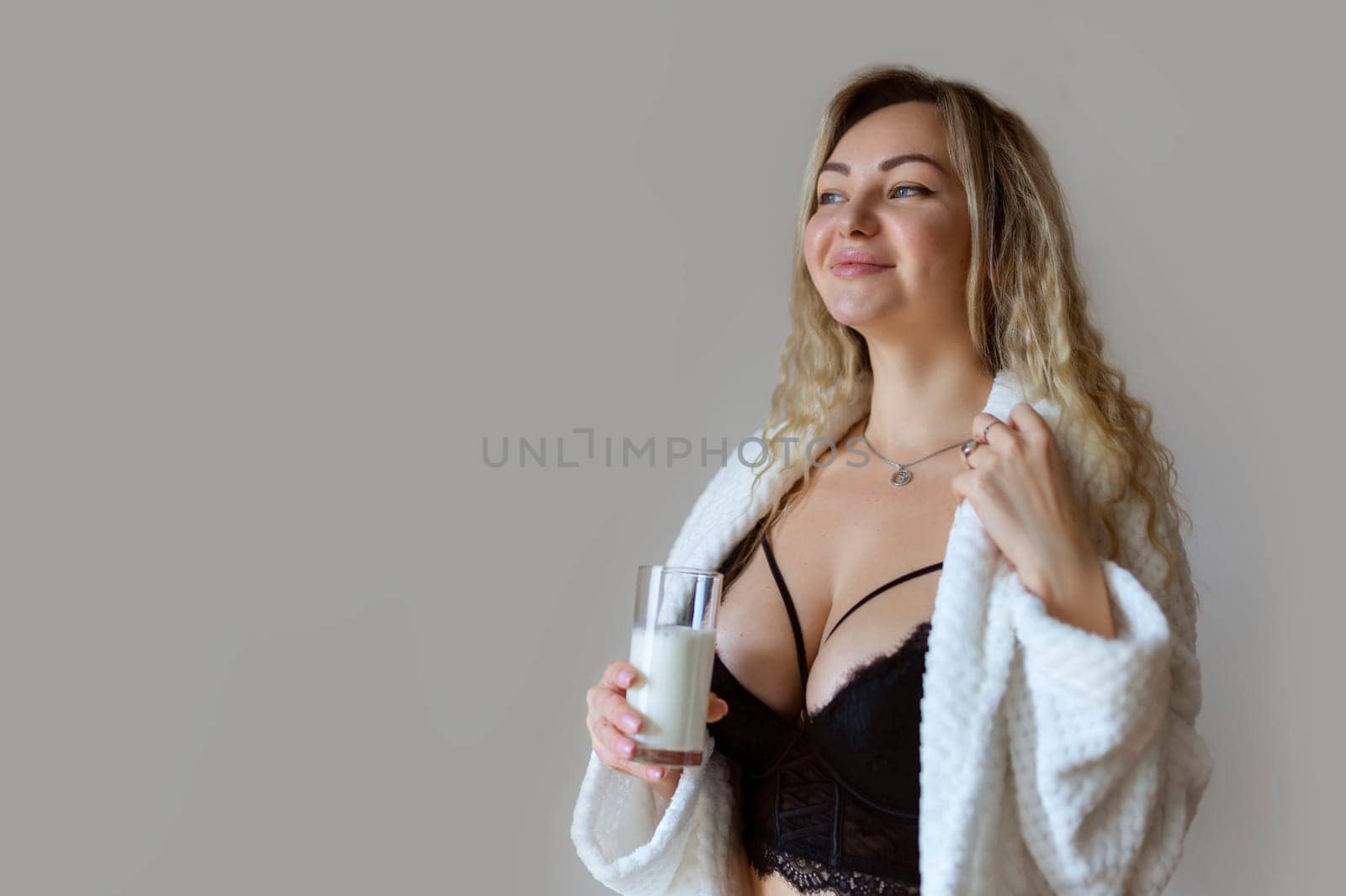 sexy young woman in black lingerie pouring milk on body isolated on grey.