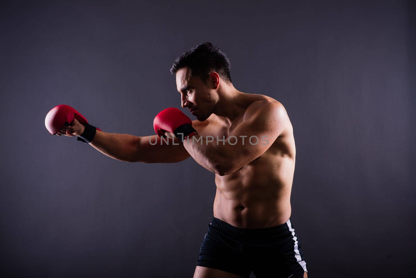 Muscular model sports young man in a boxing gloves on grey background. Male flexing his muscles.