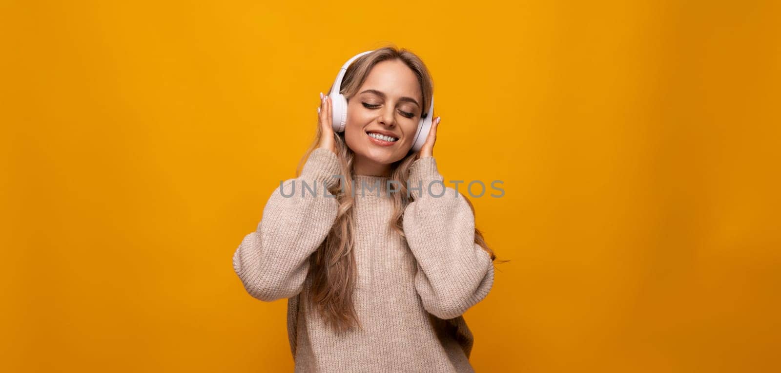 cute lady joyfully listens to music with big headphones on orange background.