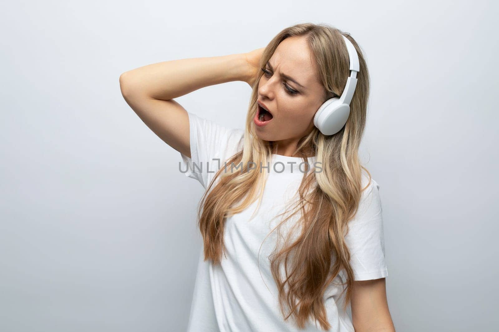 a girl with enthusiasm and joy on her face listens to music in large white headphones on a white background with empty space.