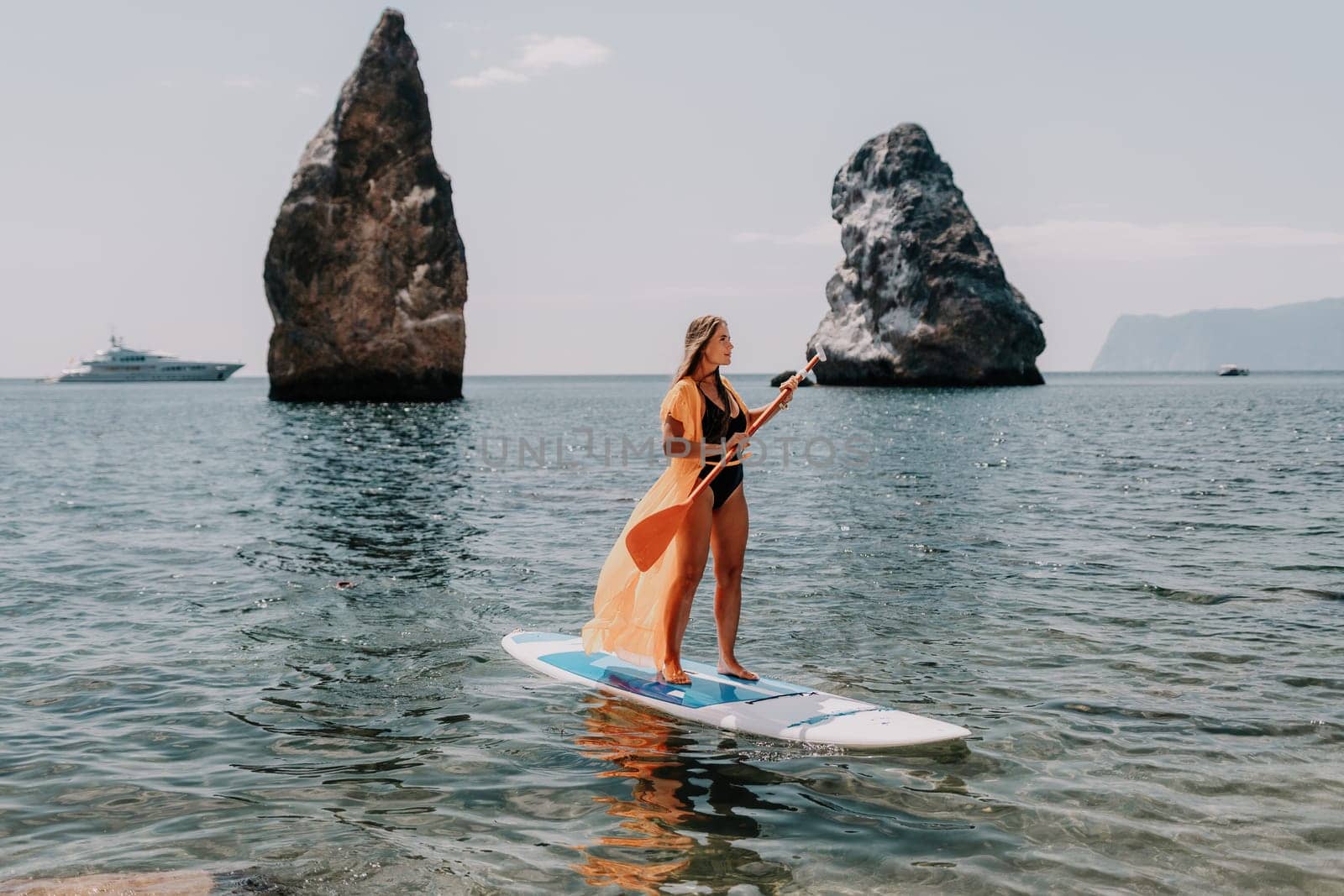 Close up shot of beautiful young caucasian woman with black hair and freckles looking at camera and smiling. Cute woman portrait in a pink bikini posing on a volcanic rock high above the sea