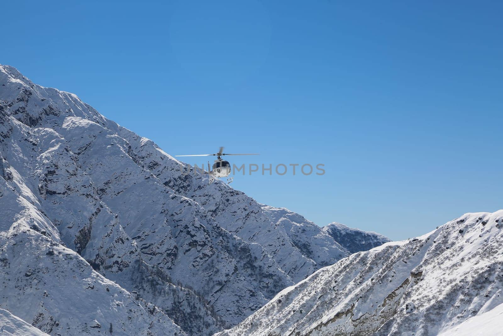 Helicopter flying in snow covered valley of Mountain in Himalaya. White helicopter on a white landscape with clear blue sky background.