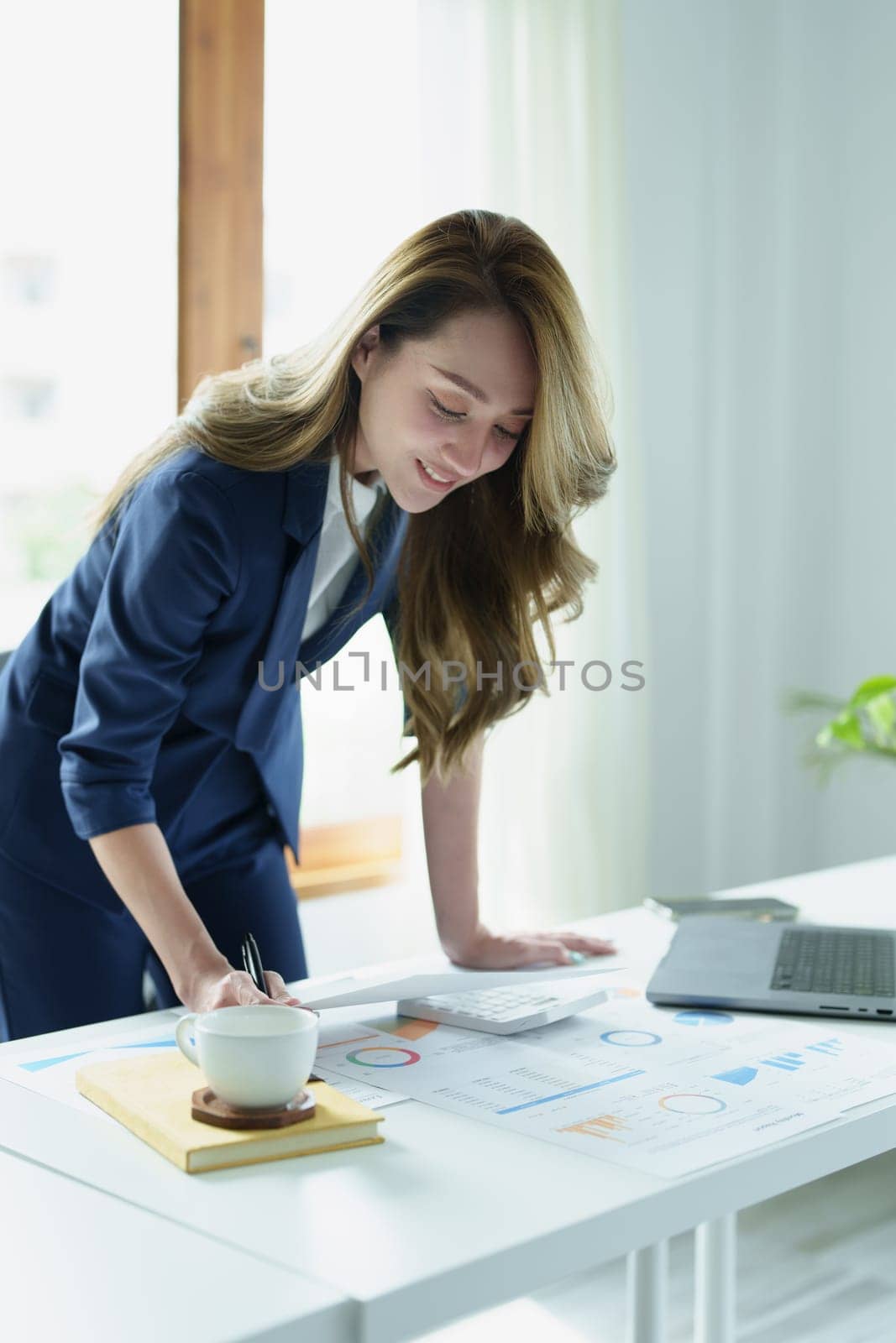 Portrait of a thoughtful Asian businesswoman looking at financial statements and making marketing plans using a computer on her desk by Manastrong