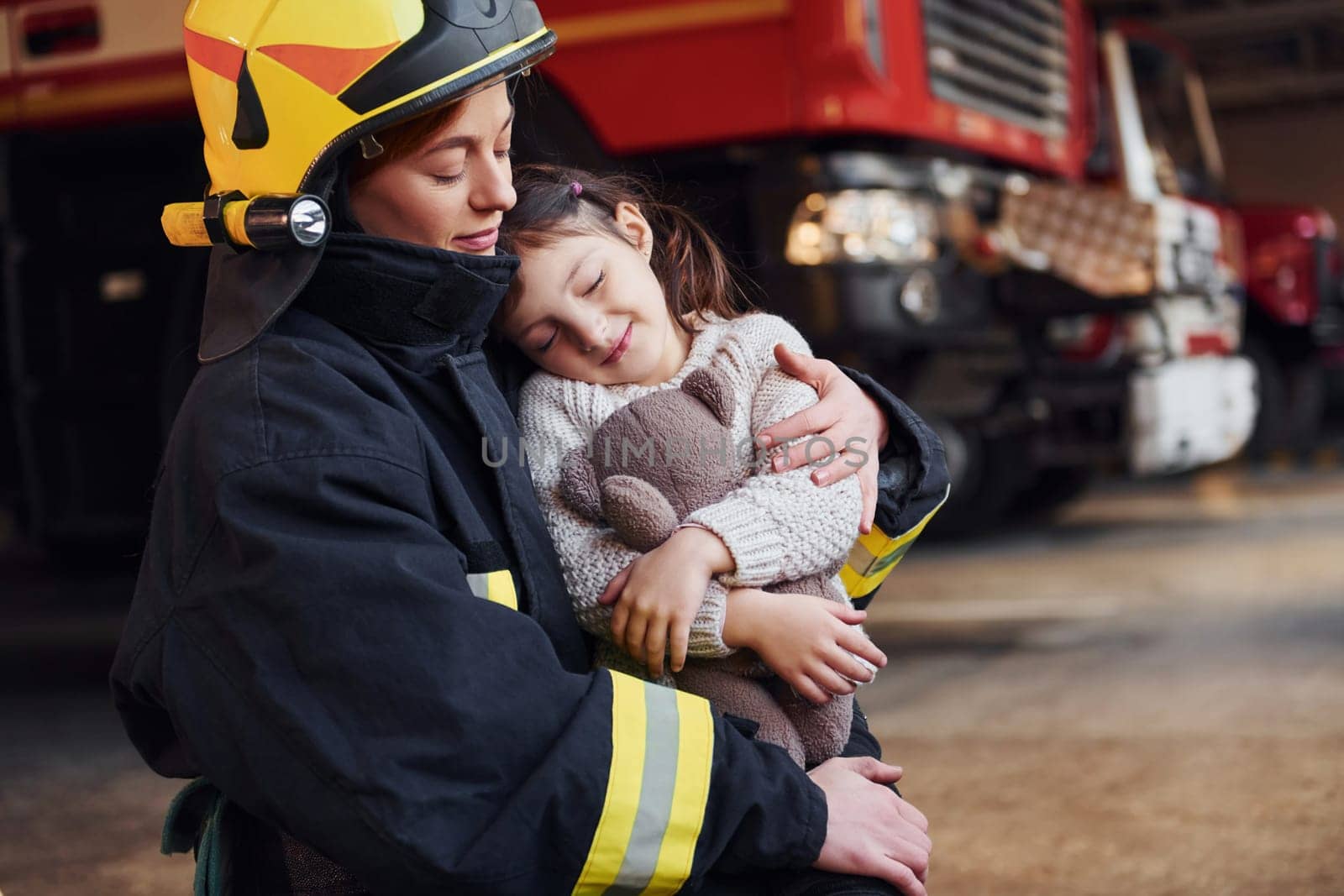 Happy little girl is with female firefighter in protective uniform.