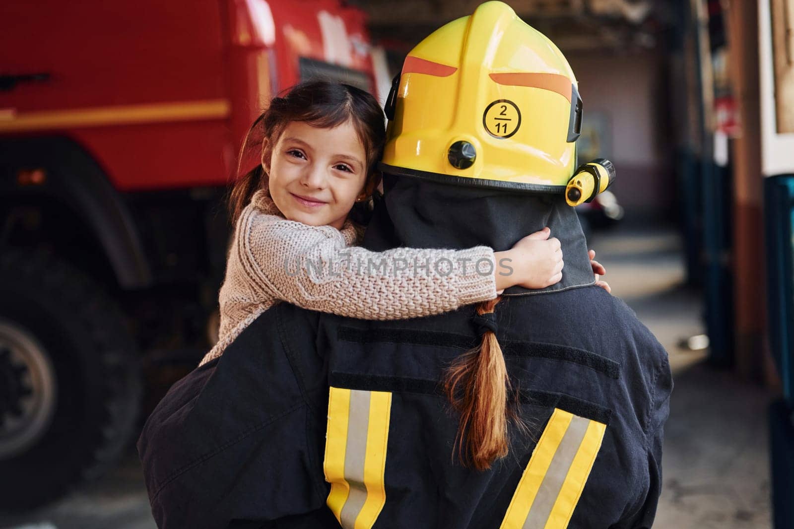 Happy little girl is with female firefighter in protective uniform.