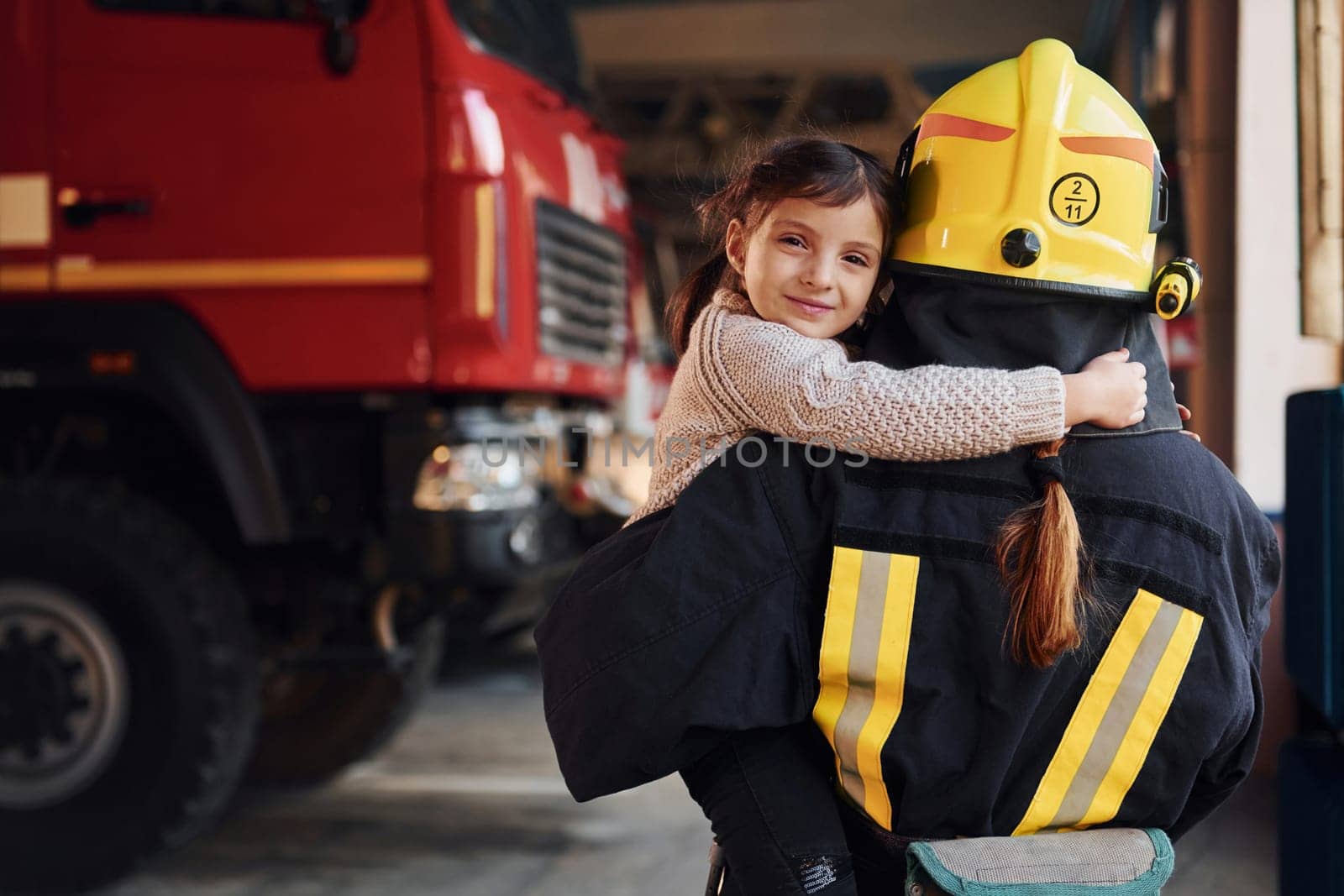 Happy little girl is with female firefighter in protective uniform.