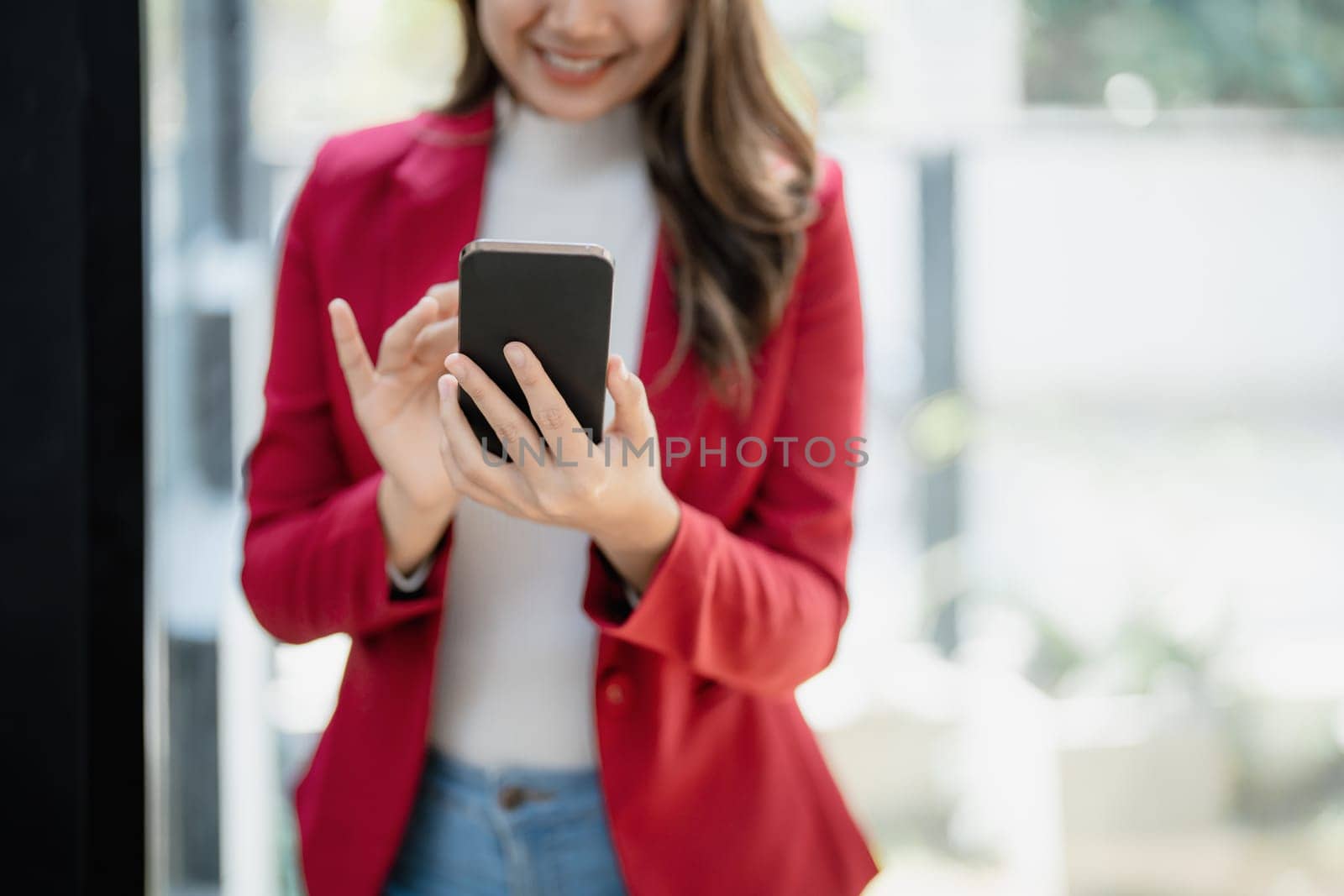 Portrait of beautiful young businesswoman standing smiling and using smartphone by Manastrong