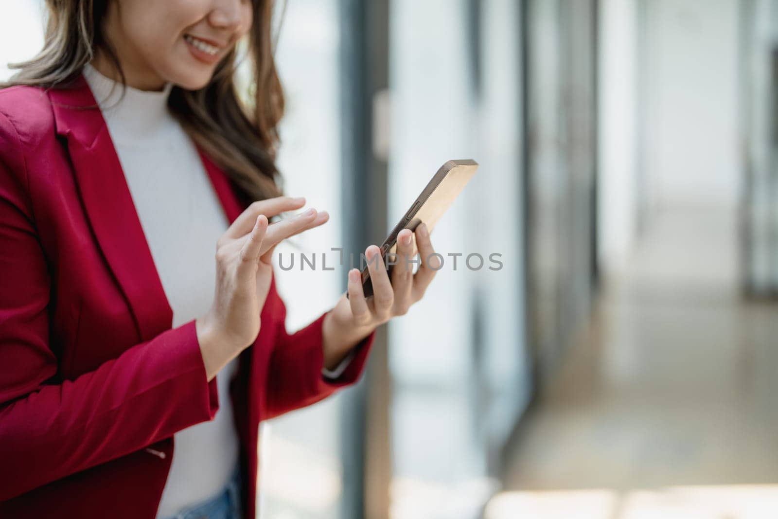 Portrait of beautiful young businesswoman standing smiling and using smartphone by Manastrong