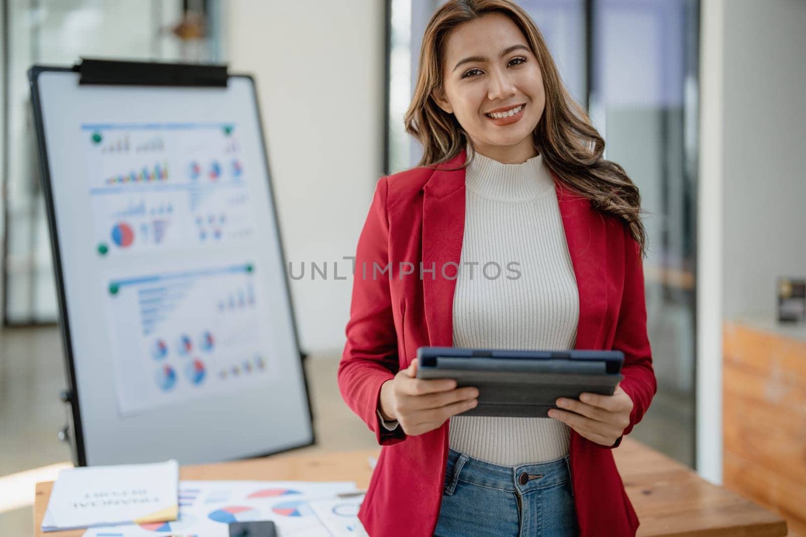 portrait of Beautiful young asian businesswoman presents business profits to colleagues at meeting, explaining business turn over on flipchart to coworkers in office with using tablet by Manastrong