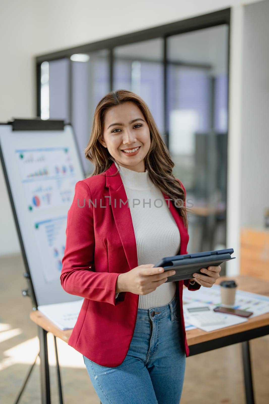 portrait of Beautiful young asian businesswoman presents business profits to colleagues at meeting, explaining business turn over on flipchart to coworkers in office with using tablet by Manastrong