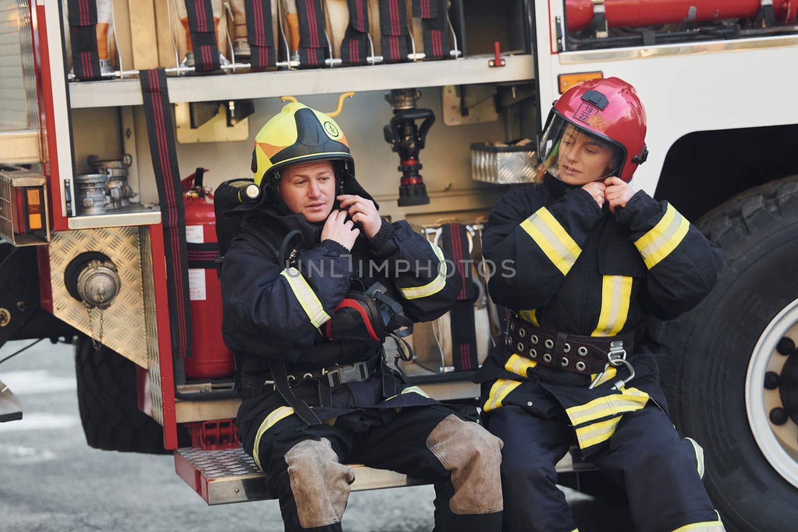 Male and female firefighters in protective uniform is outdoors together.