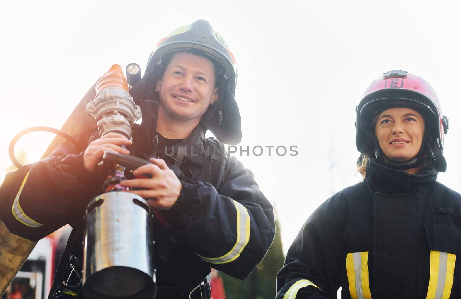 Male and female firefighters in protective uniform is outdoors together.
