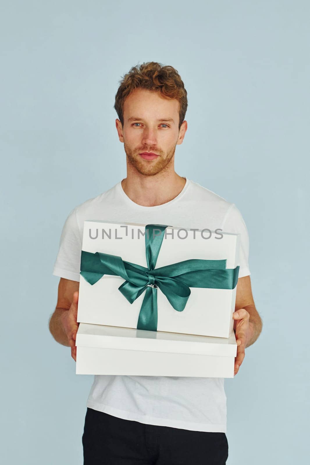 Young man in white shirt standing against wall and holds gift box.