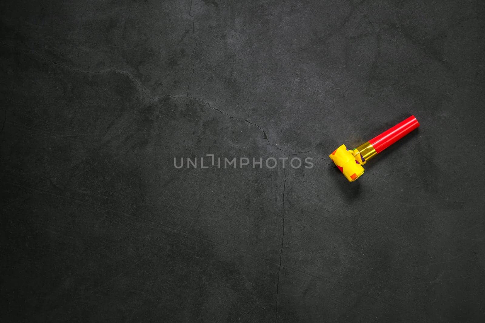 Birthday party blowouts whistles Rolled festive noisemaker or party whistle on concrete dark background, blowing in whistle top view in and out loop 4k Happy Birthday copy space
