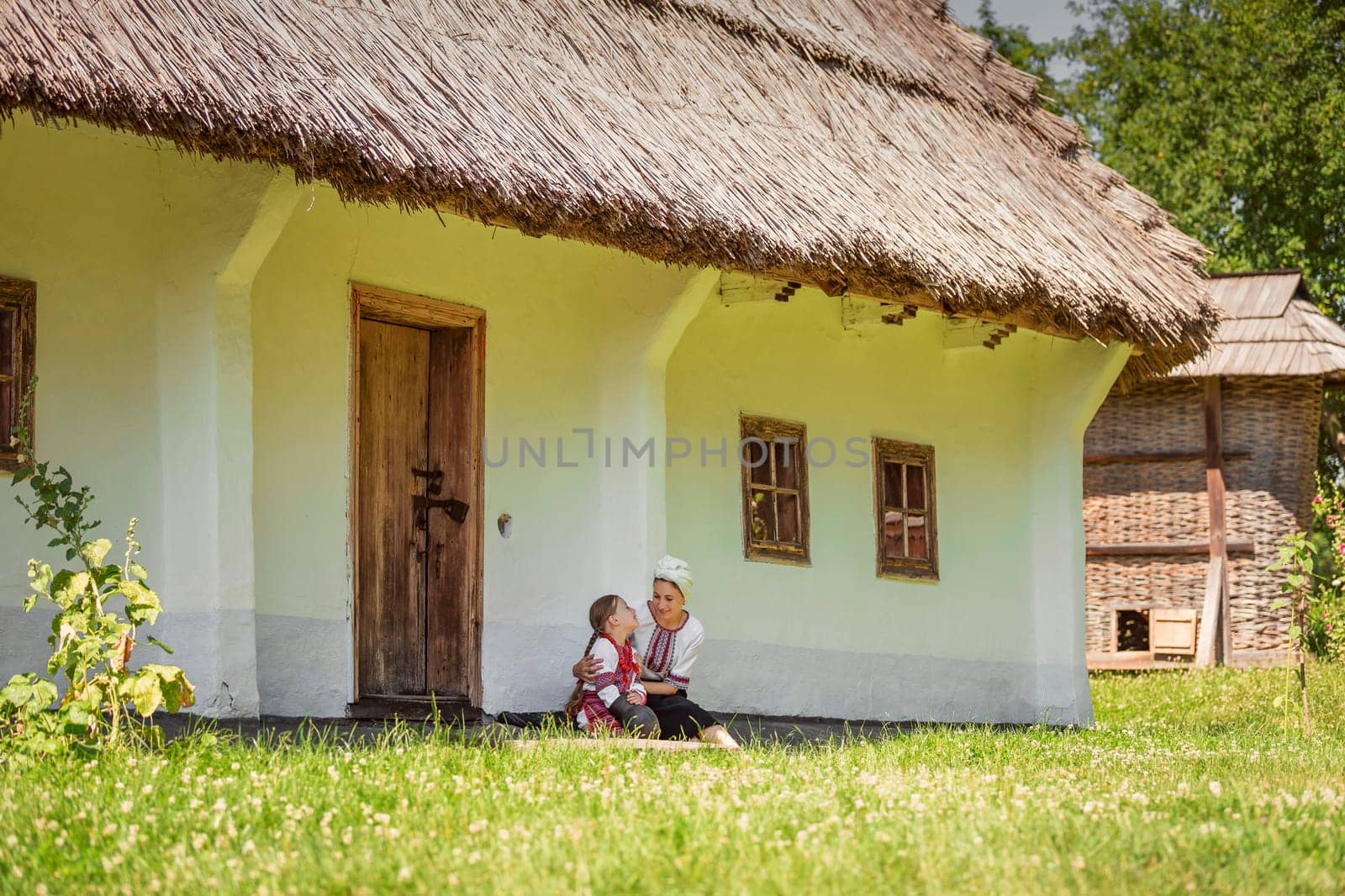 mother and daughter in traditional Ukrainian clothes are sitting near the house