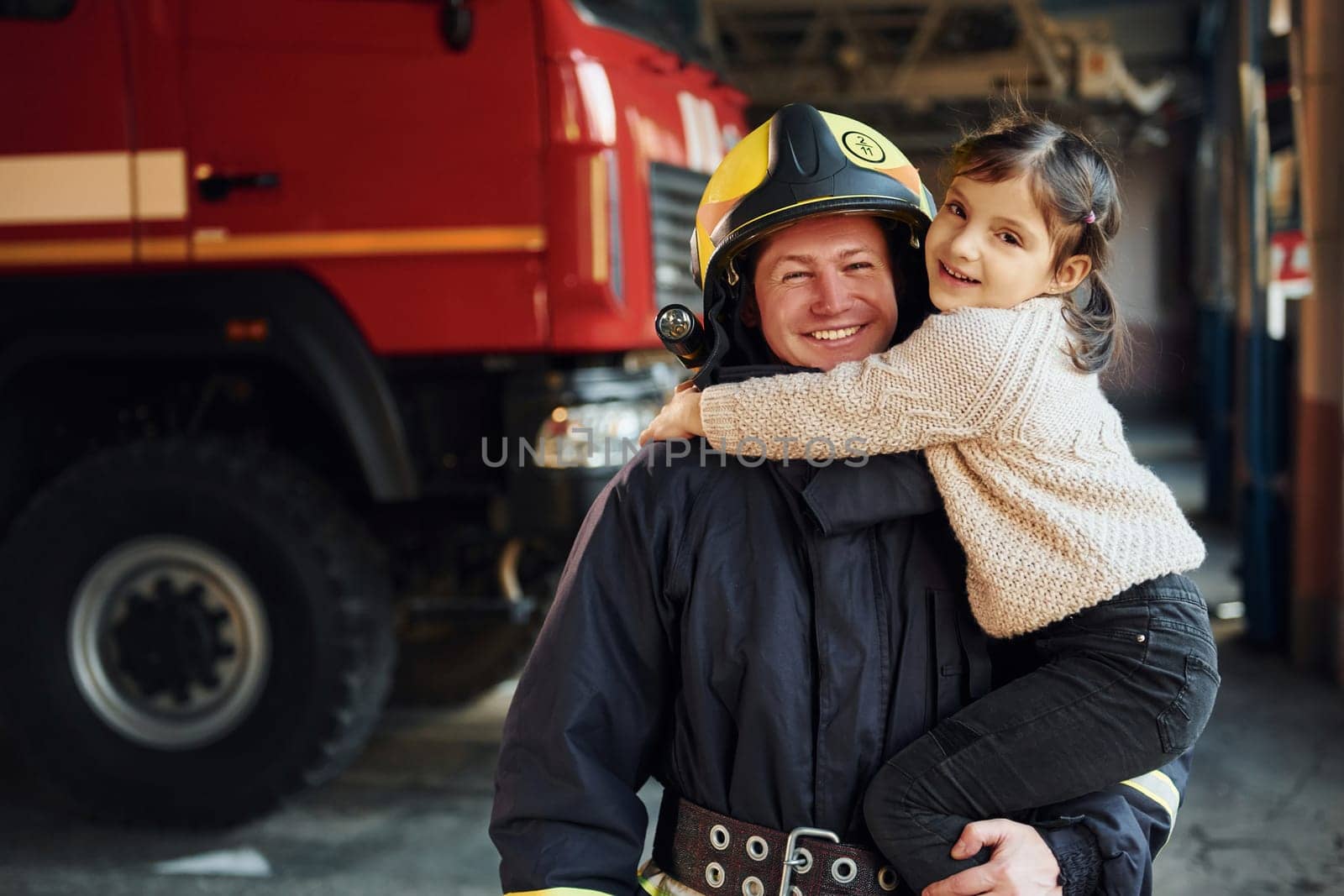 Happy little girl is with male firefighter in protective uniform.