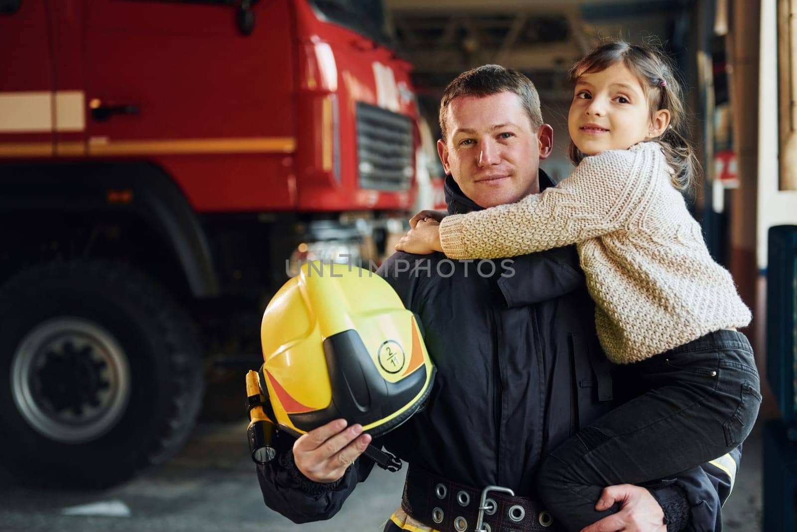 Happy little girl is with male firefighter in protective uniform.