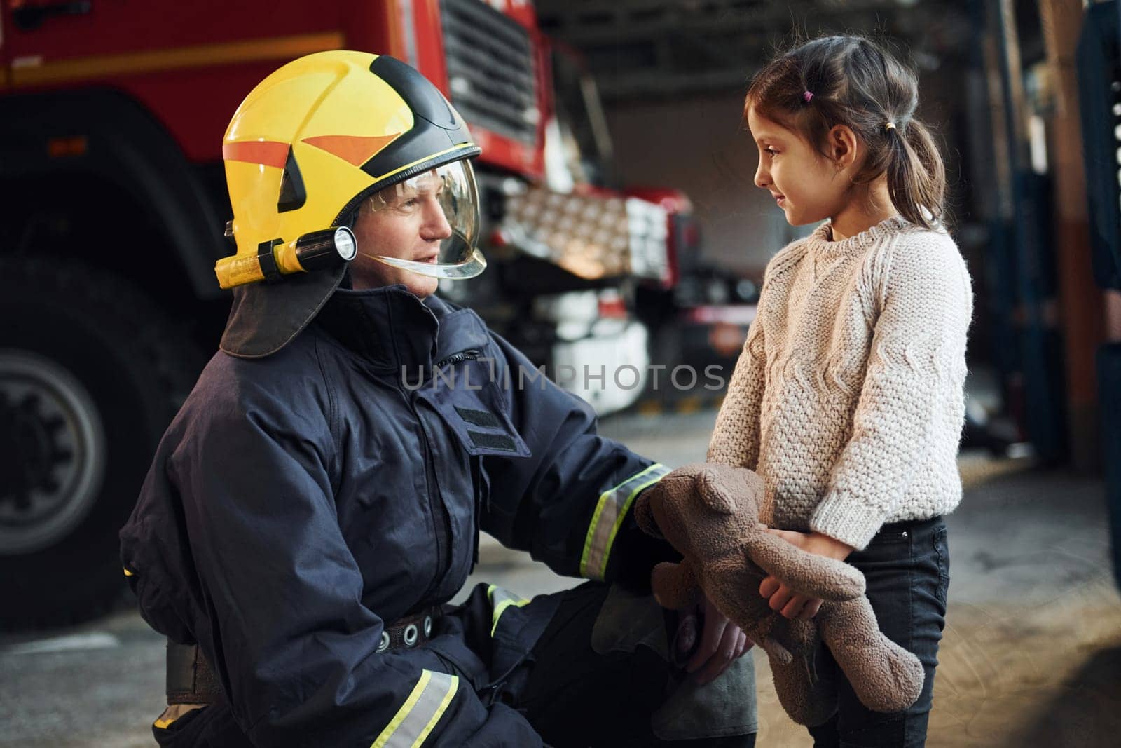 Happy little girl is with male firefighter in protective uniform.