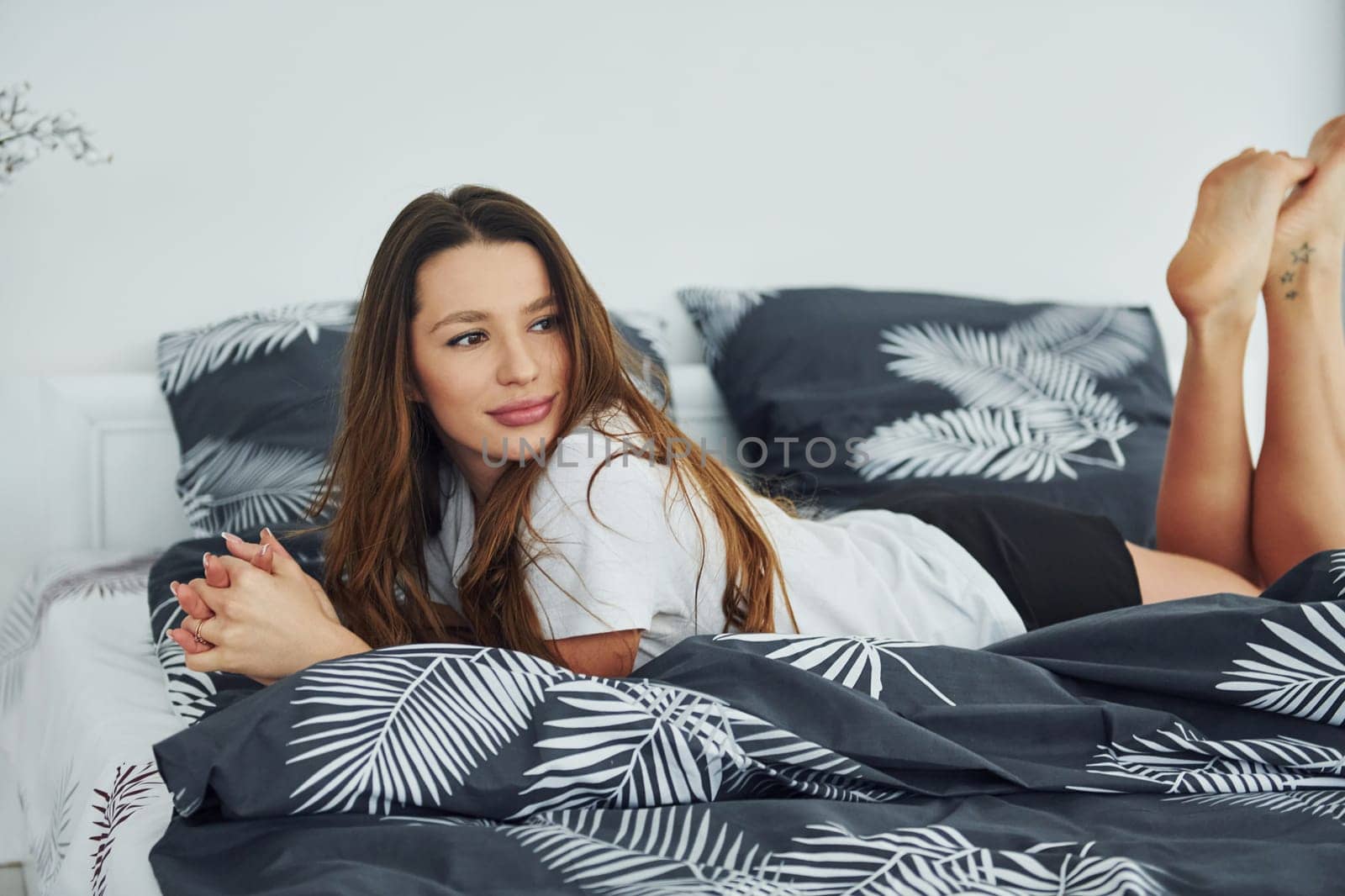 Front view of happy relaxed woman on bed. Interior and design of beautiful modern bedroom at daytime.