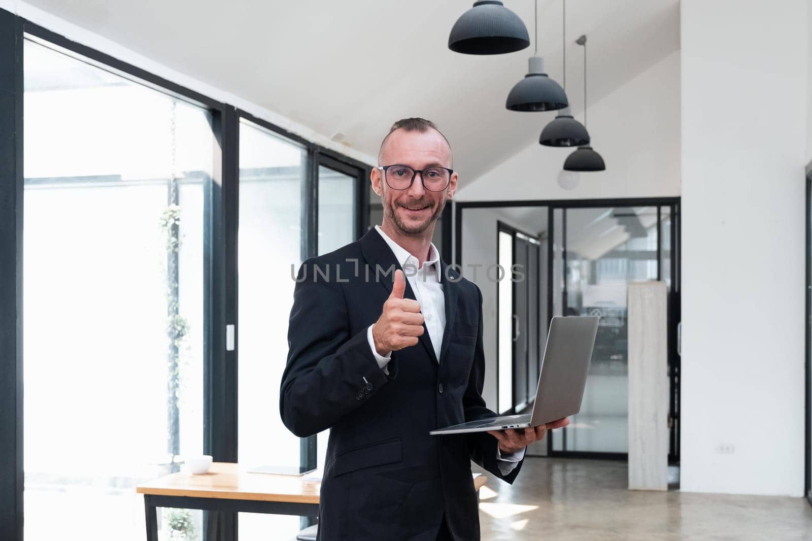 Young business smiling handsome man holding laptop computer with thumb up standing in office..