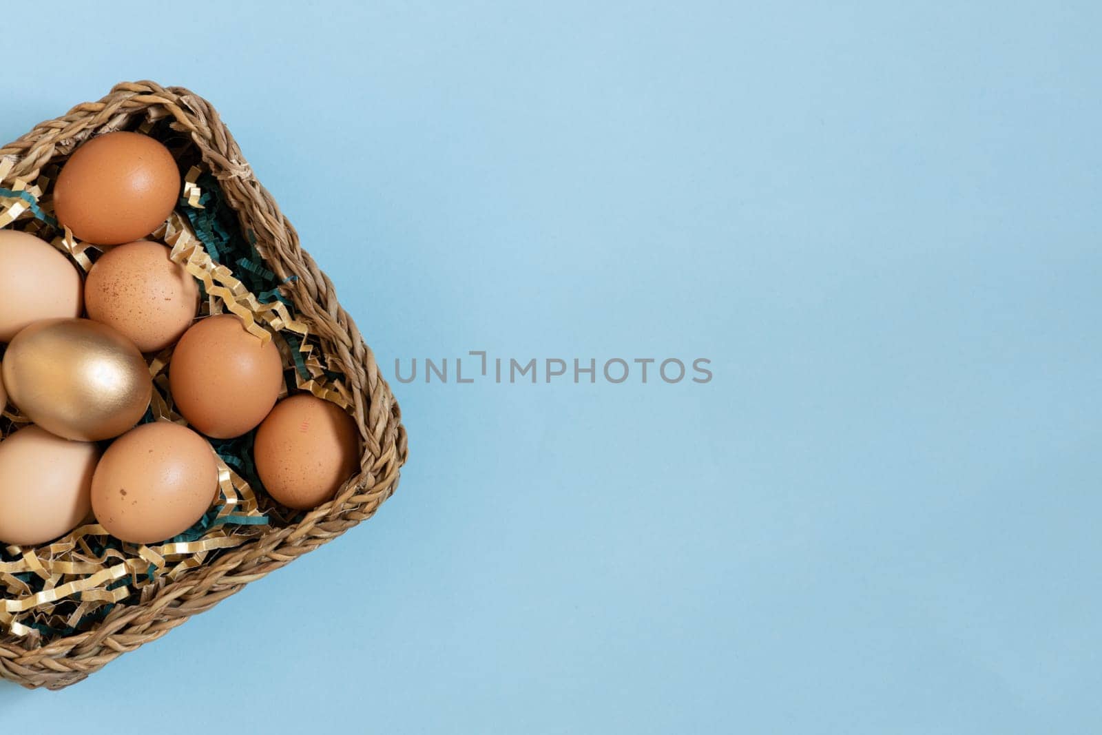 Gift basket with easter eggs, golden and natural color eggs in basket. Top view on eggs above pastel blue background. by Ri6ka