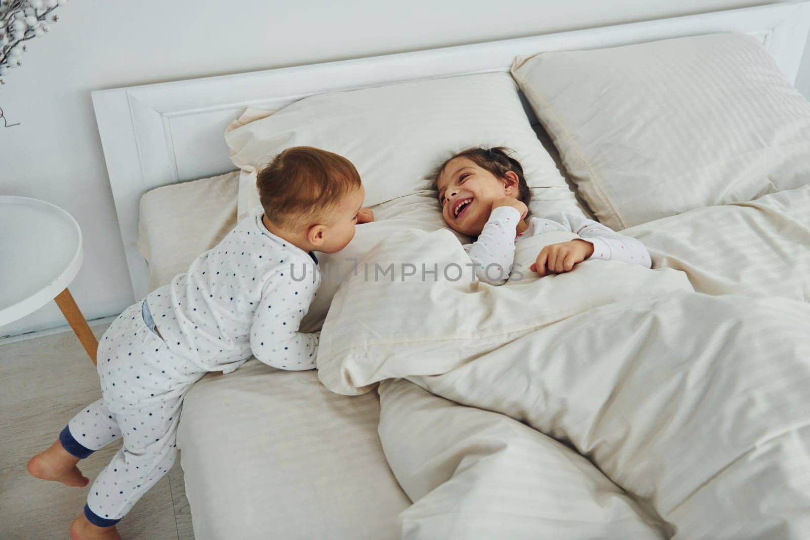 Two kids have fun while liyng down on bed. Interior and design of beautiful modern bedroom at daytime.