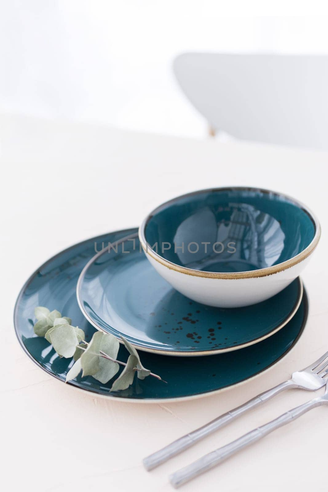 Three empty green plates with silver cutlery on white table in front of window. Set of three various plates on table. Minimal style table setting