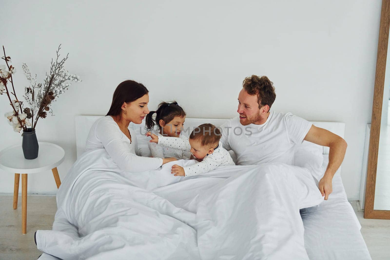 Woman and man lying down on bed with their children. Interior and design of beautiful modern bedroom at daytime.