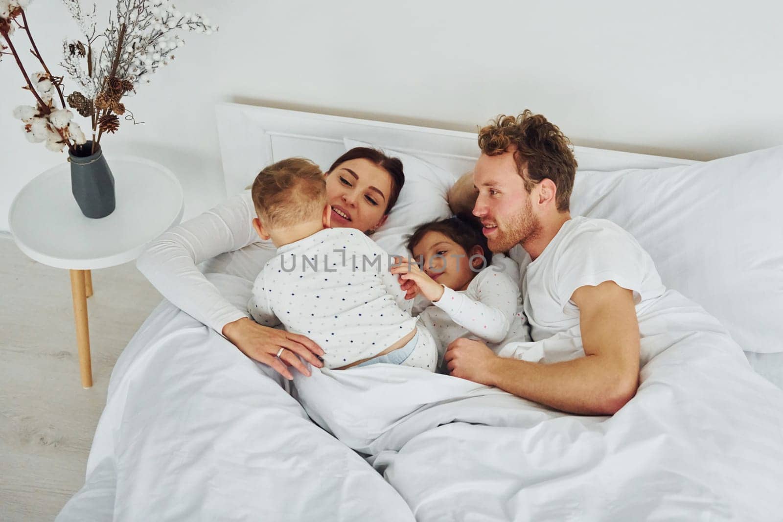 Woman and man lying down on bed with their children. Interior and design of beautiful modern bedroom at daytime.