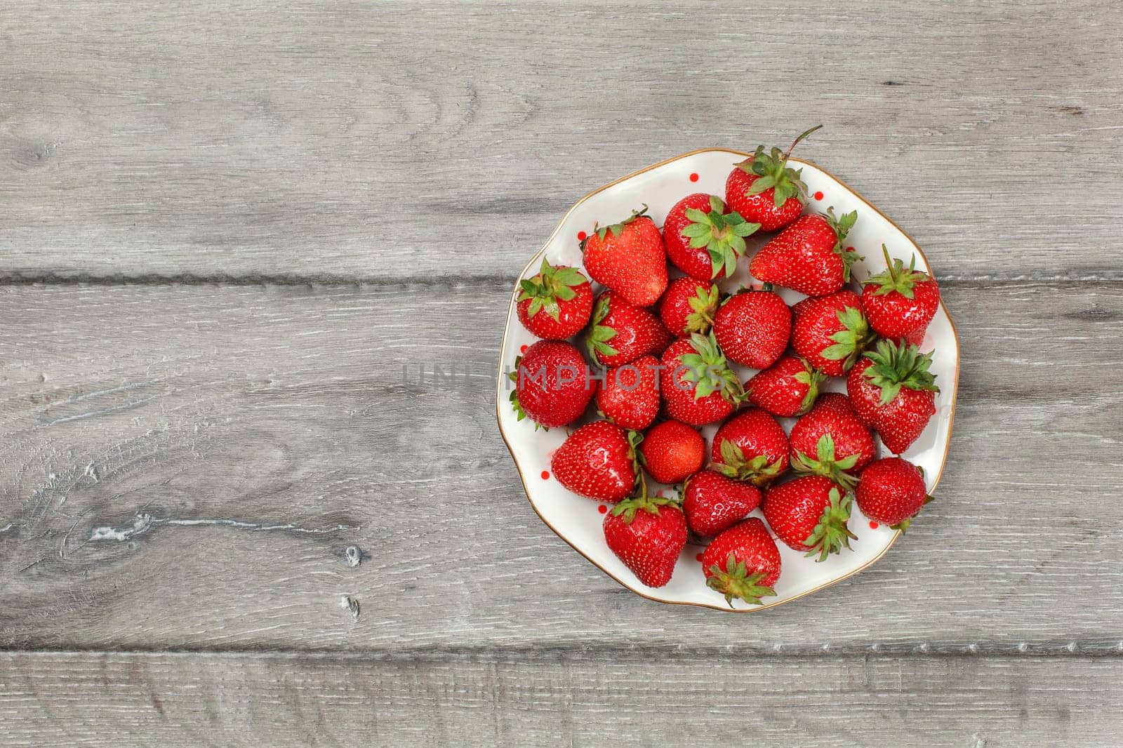 Tabletop view, plate with strawberries on gray wood desk. Space for text on left.