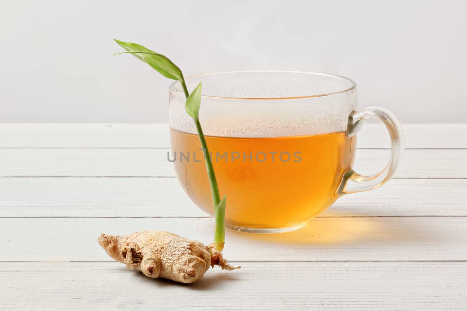 Glass of freshly brewed tea, dry ginger root with green sprout next to it.