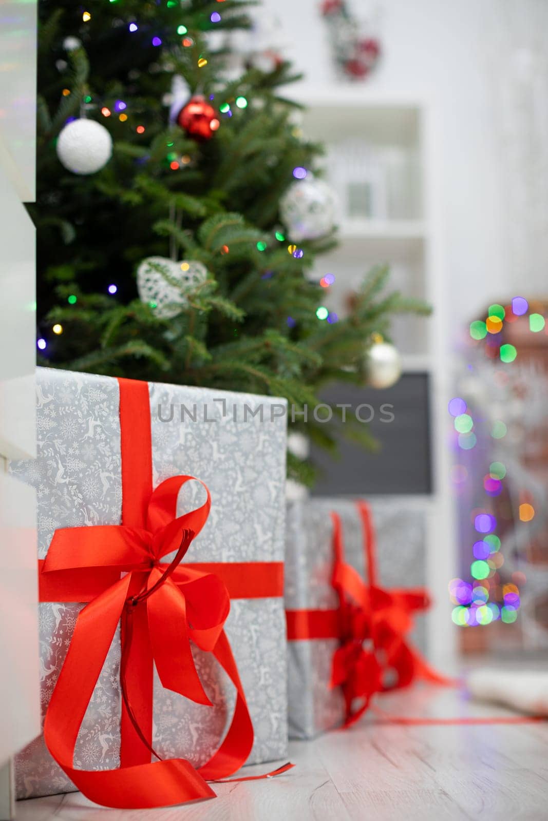 Elegant package on a bright floor. Silver gifts with red ribbons under Christmas tree.