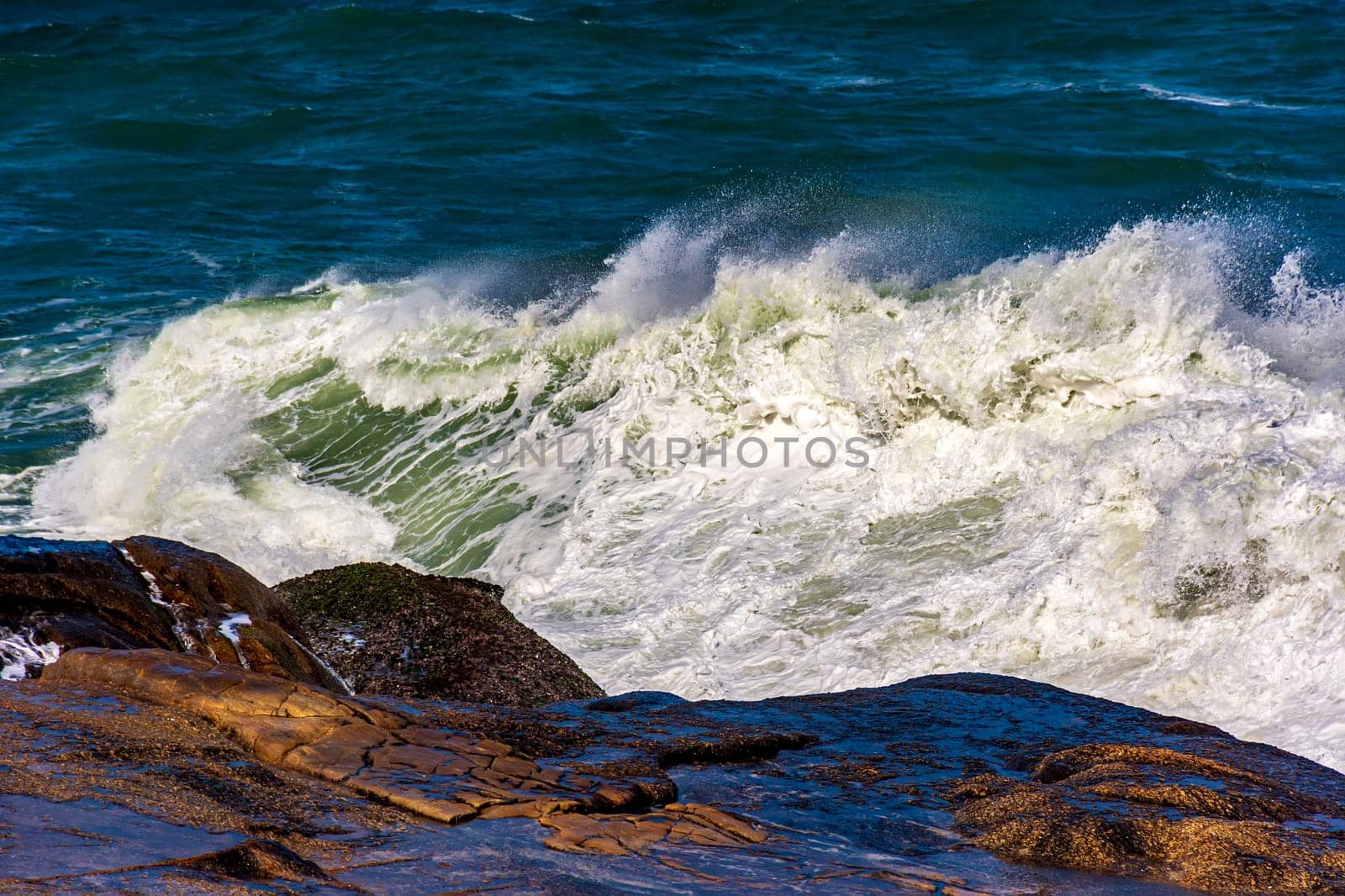 Beautiful sea waves crashing against the rocks with water drops and foam splashing in the air on a sunny day