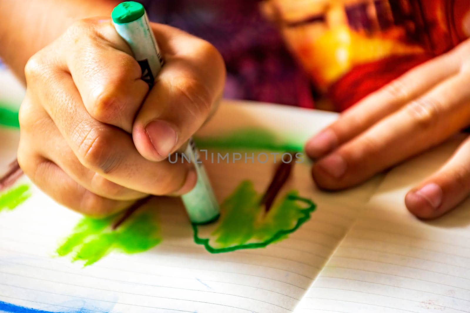 Child's hands drawing with crayon on a sheet of paper illuminated by the side light from the window