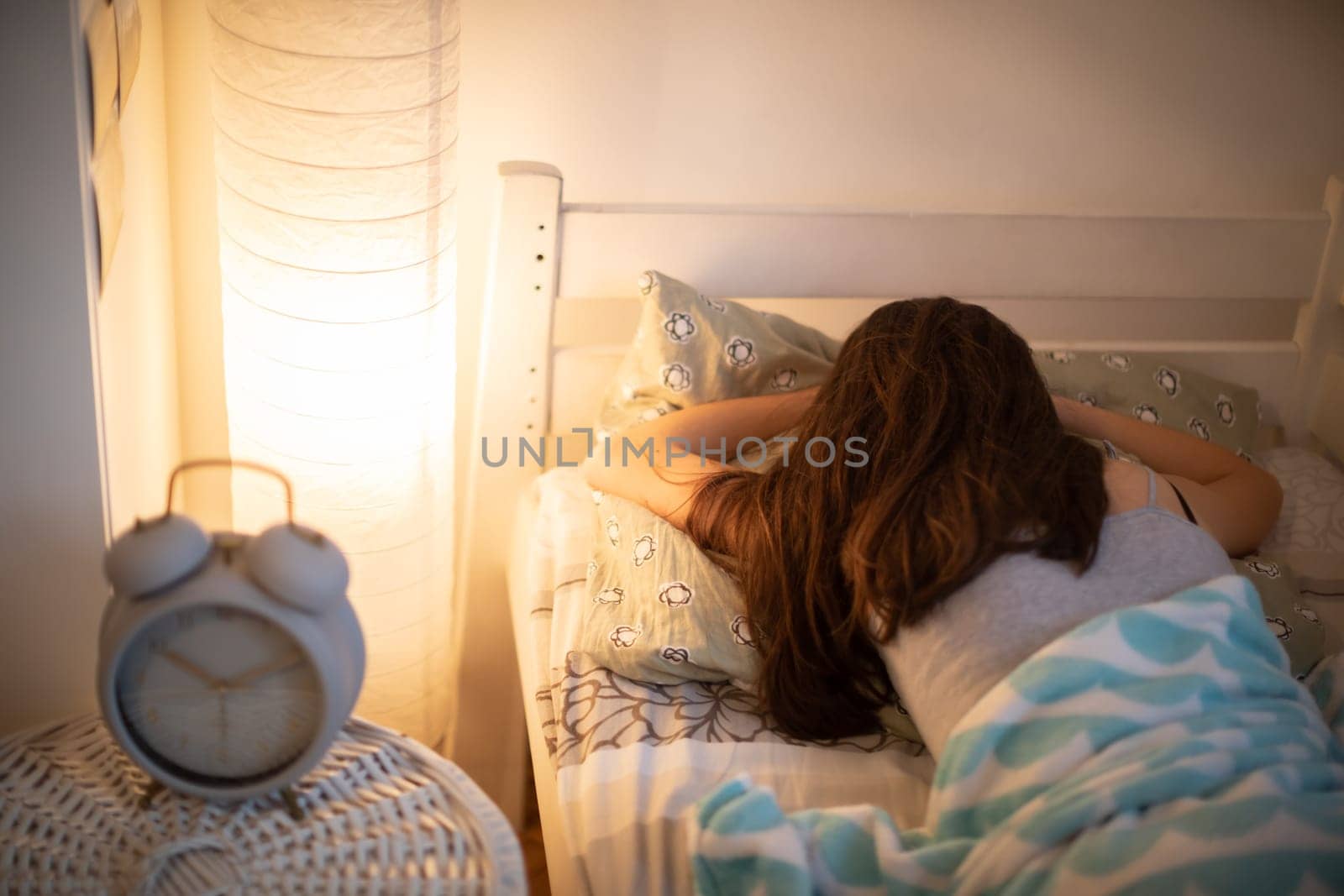 The alarm clock stands on the cabinet next to the bed in which the woman sleeps with the bedside lamp lit. It is already 10 minutes past 10 o'clock on the clock.