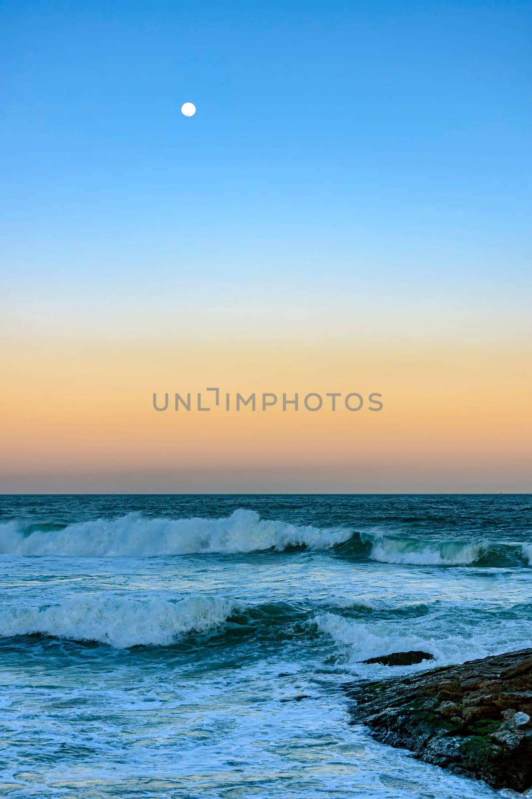 Moon over the sea and waves during sunset at Ipanema beach in Rio de Janeiro, Brazil