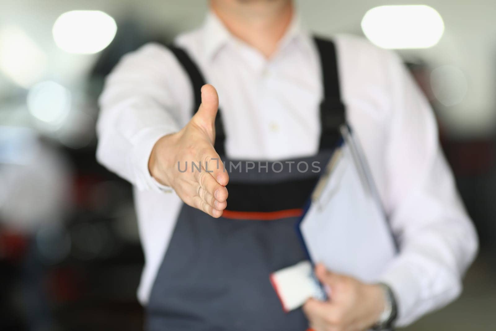 Closeup of auto mechanic greeting and offering handshake while working in an auto repair shop by kuprevich