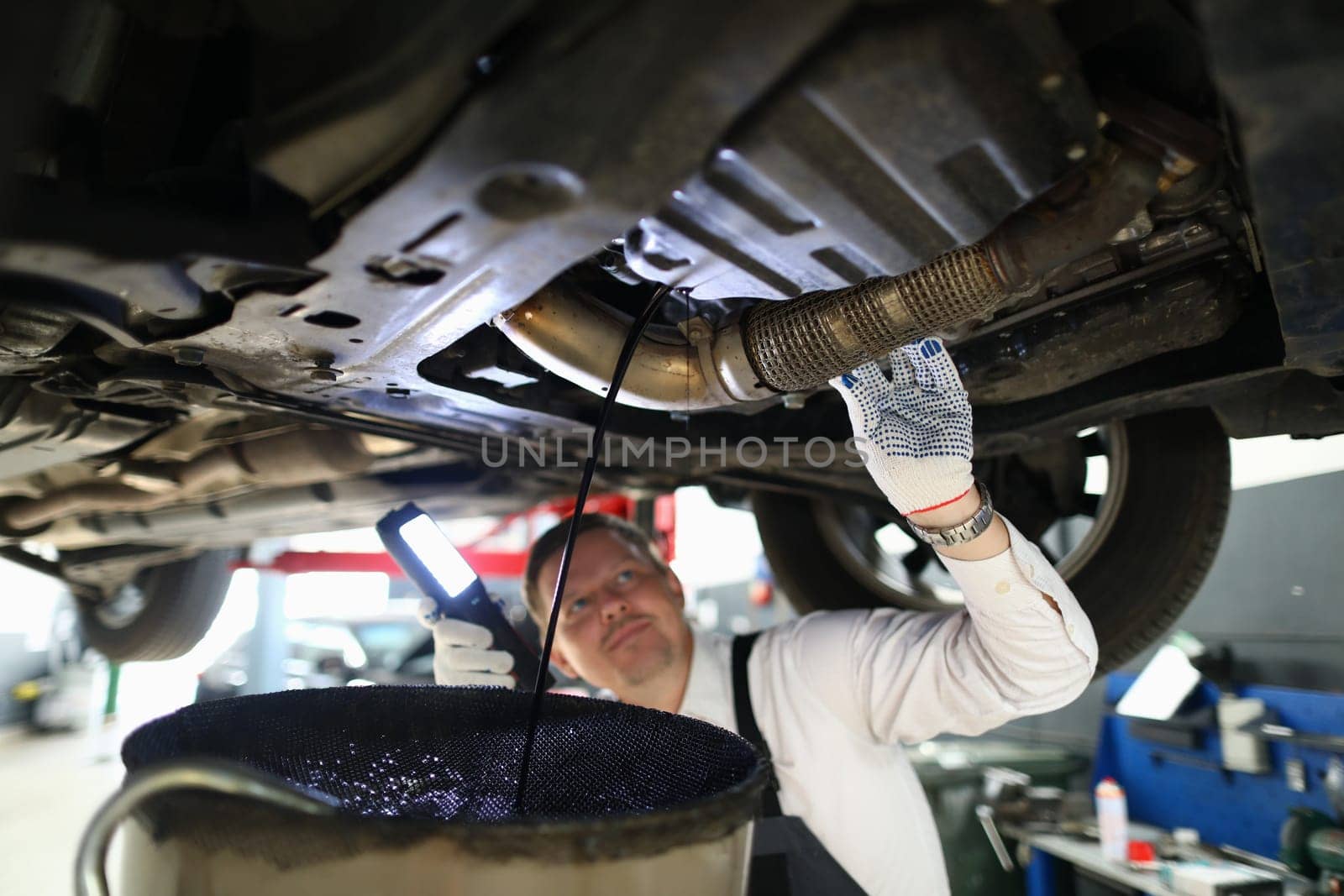 Mechanic with a lamp inspects suspension of car on lift by kuprevich