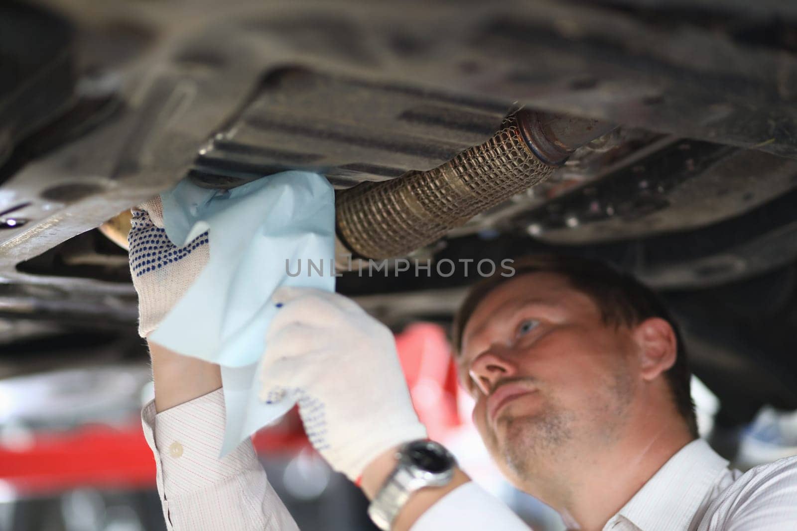 Auto mechanic inspects car leak and suspension parts of raised car with napkin at repair station. Service and repair auto concept