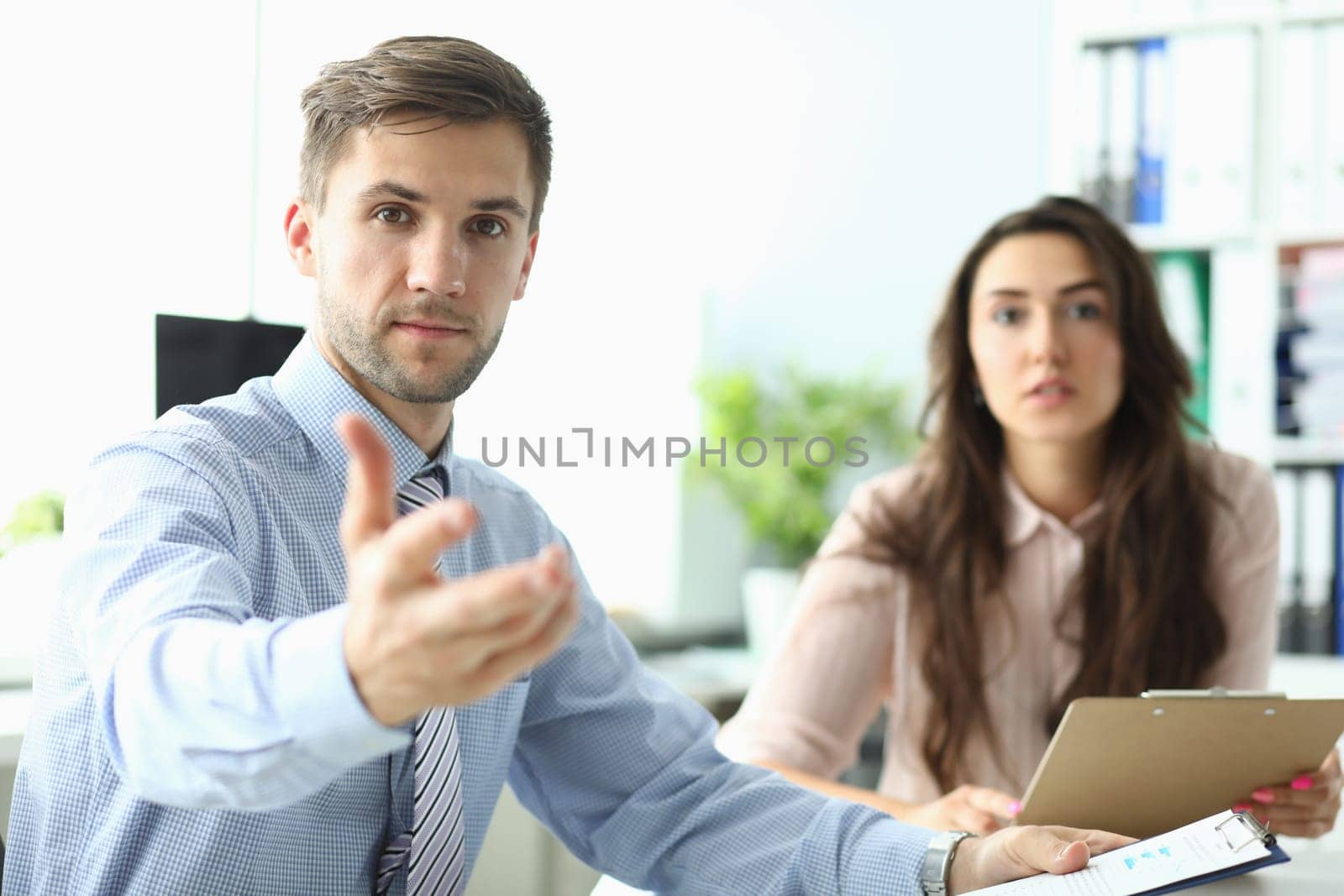 Businessman with woman stretches his hands forward sitting in office. Business consultant concept