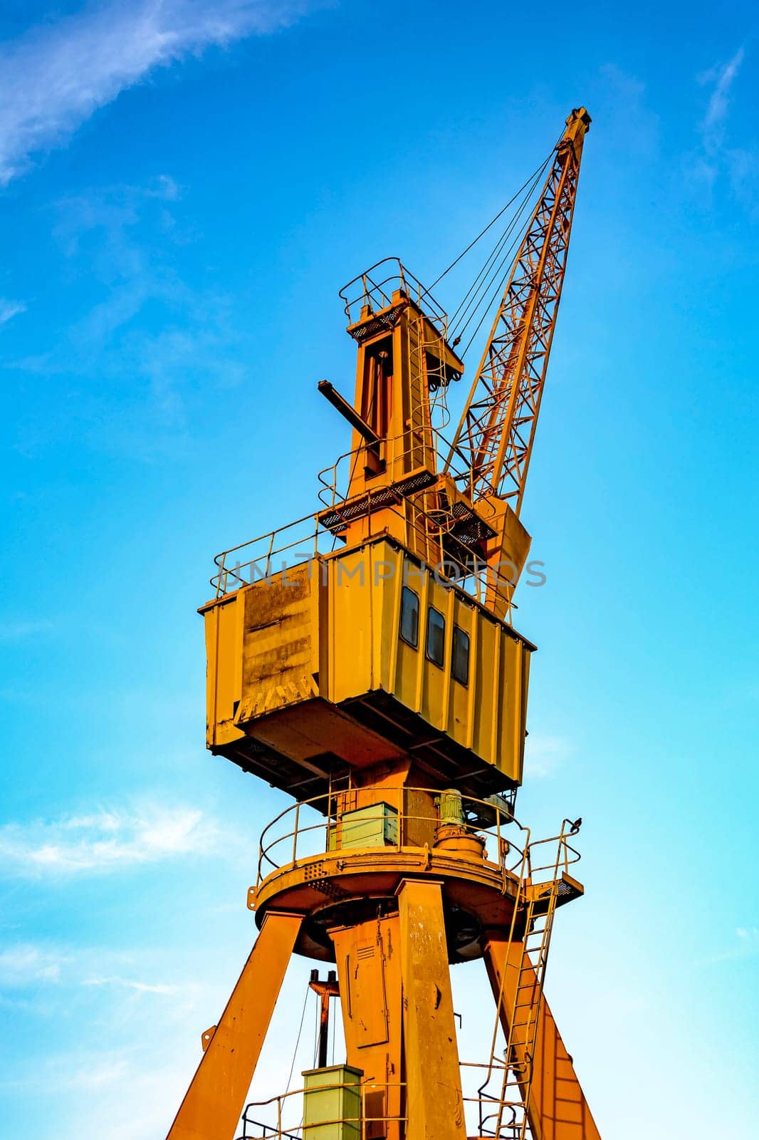 Old and obsolete yellow crane on the harbor pier with blue sky in the background.