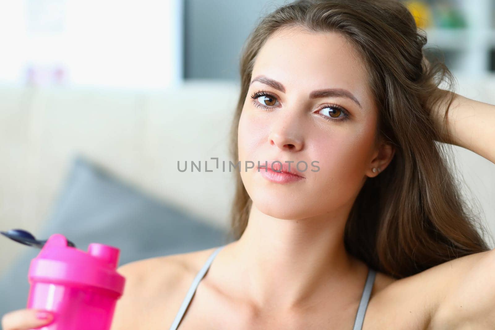 Portrait of fit woman in sportswear holding shaker with whey protein or fresh water. Workout and home fitness for health concept