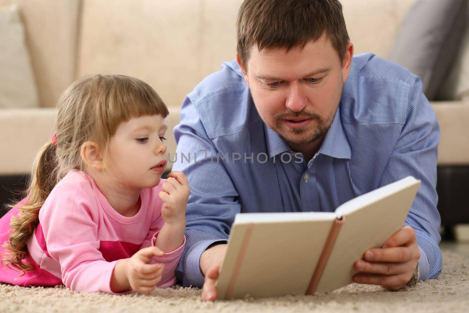 Loving dad lies on warm floor in living room with cute little daughter. Caring father enjoying fairy tale with happy child concept
