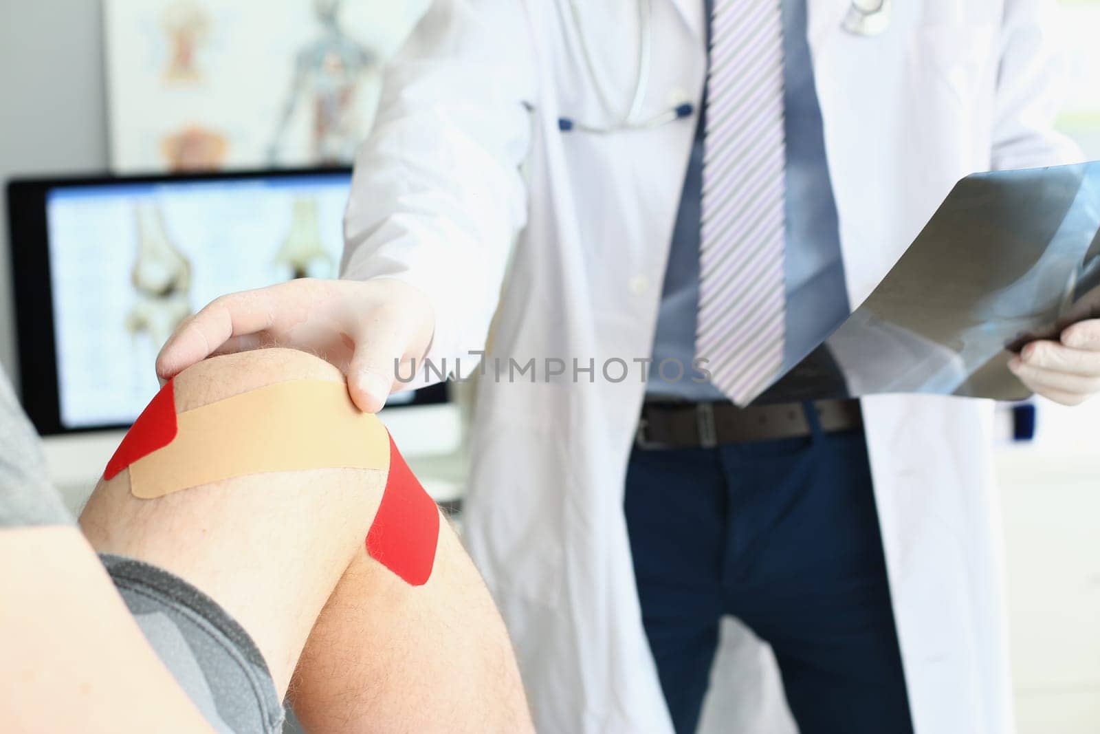 Physiotherapist applying kinesiology tape to male patient knee by kuprevich